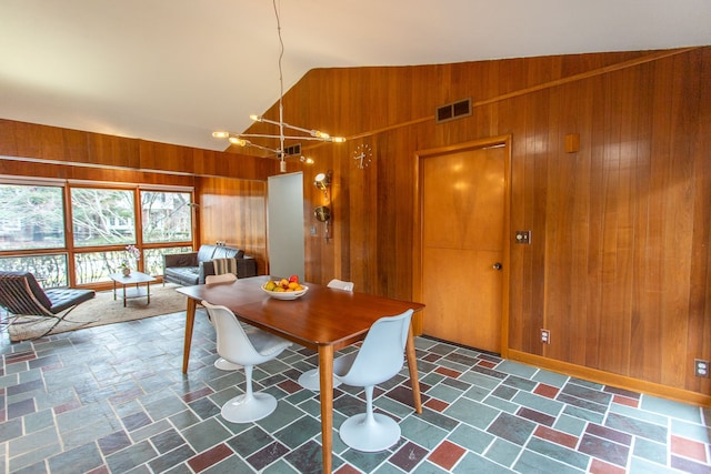 dining space featuring lofted ceiling, stone finish floor, visible vents, and wooden walls