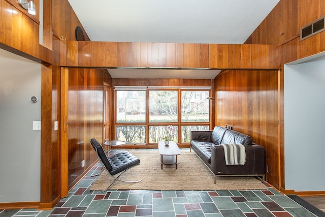 unfurnished living room featuring visible vents, wood walls, and baseboards