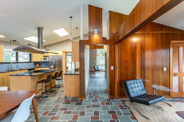 kitchen featuring white microwave, wooden walls, a sink, vaulted ceiling, and stainless steel fridge