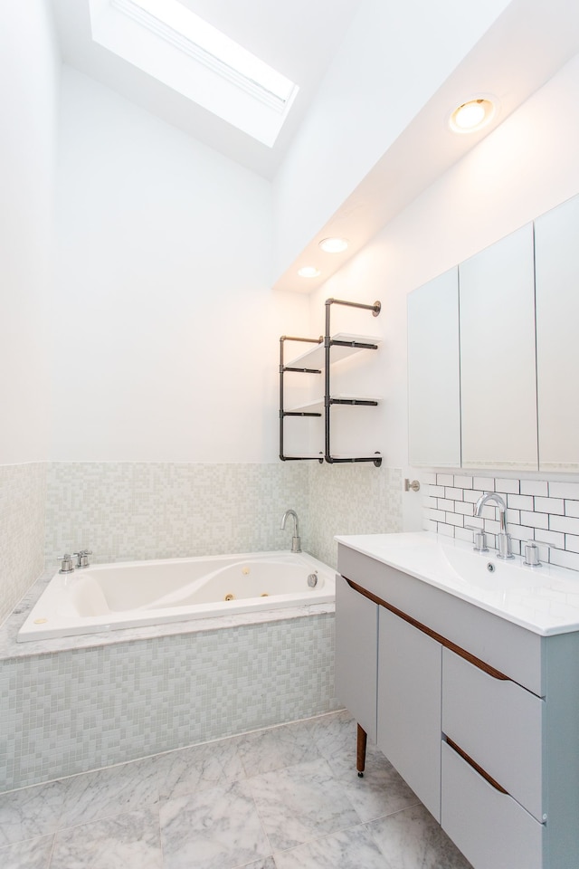 bathroom featuring lofted ceiling with skylight, marble finish floor, vanity, and a whirlpool tub