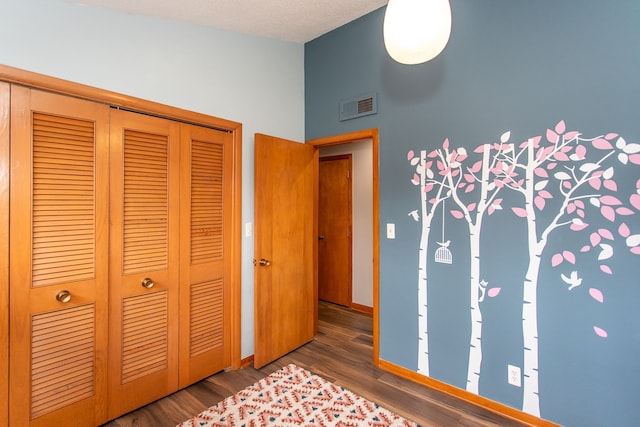 unfurnished bedroom featuring dark wood-style floors, a closet, visible vents, and baseboards