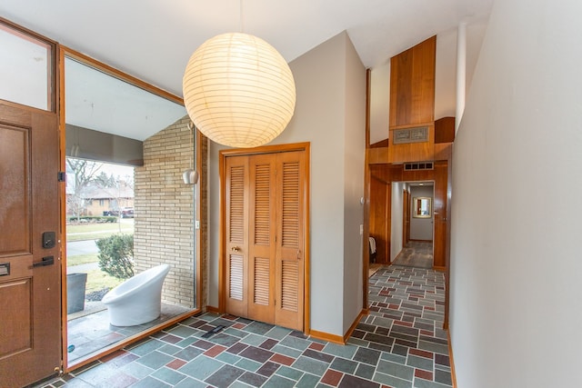 foyer entrance featuring lofted ceiling, stone finish flooring, visible vents, and baseboards