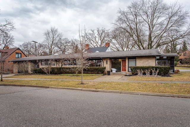 view of front facade with brick siding, a chimney, and a front lawn