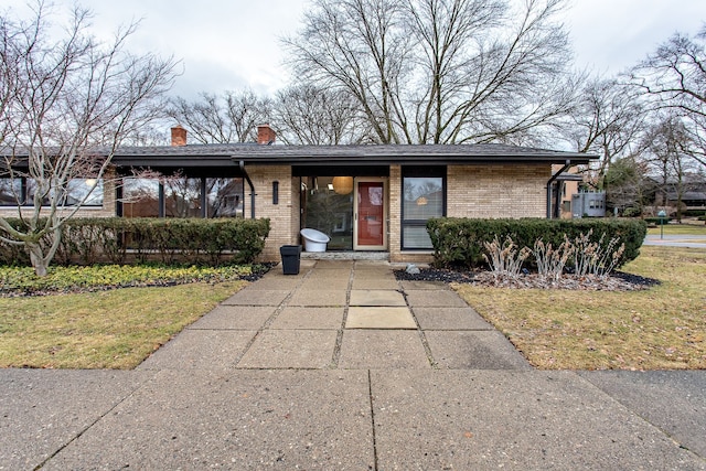 mid-century home featuring brick siding, a chimney, and a front lawn