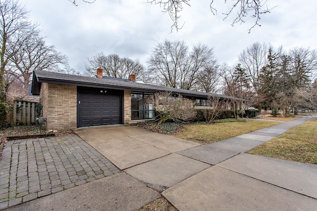 view of front of home with an attached garage, brick siding, concrete driveway, a chimney, and a front yard