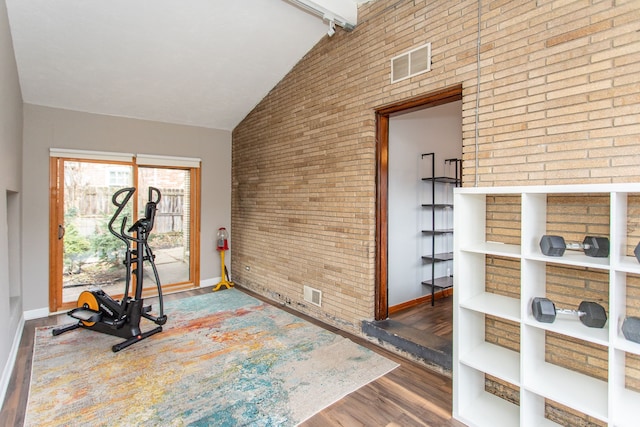 exercise room featuring high vaulted ceiling, visible vents, brick wall, and wood finished floors