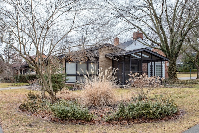 view of front of house featuring a sunroom, brick siding, and a chimney