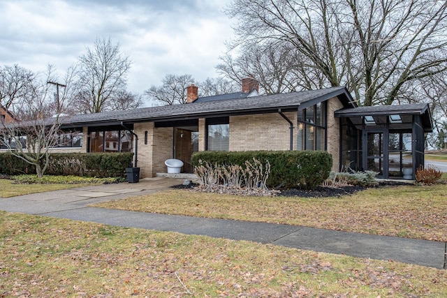 mid-century modern home featuring brick siding, a chimney, a front yard, and a sunroom