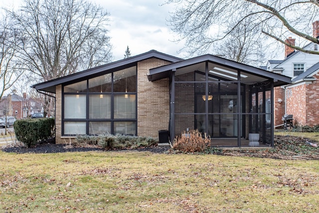 rear view of property featuring a yard, brick siding, and a sunroom