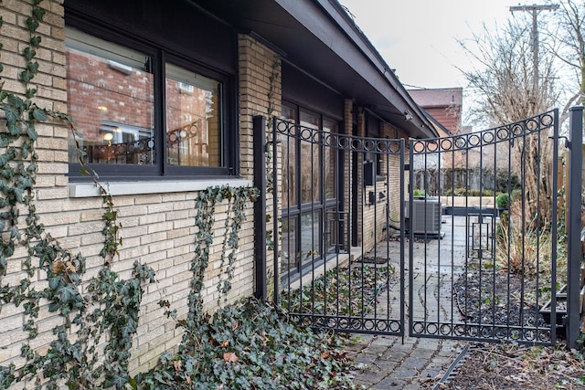 view of property exterior with central AC, brick siding, and a gate