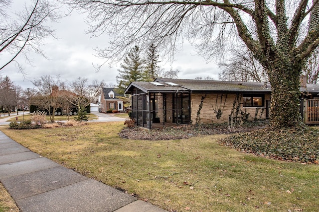 view of side of home with brick siding, a lawn, and a sunroom