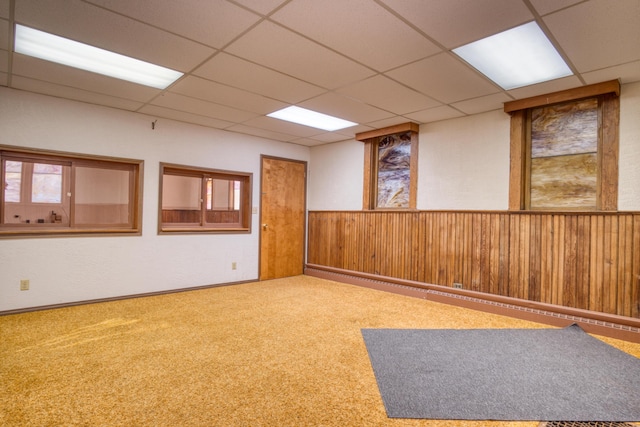 empty room featuring carpet floors, wainscoting, a paneled ceiling, and wooden walls