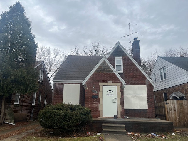 view of front of property with brick siding, a chimney, a shingled roof, and fence