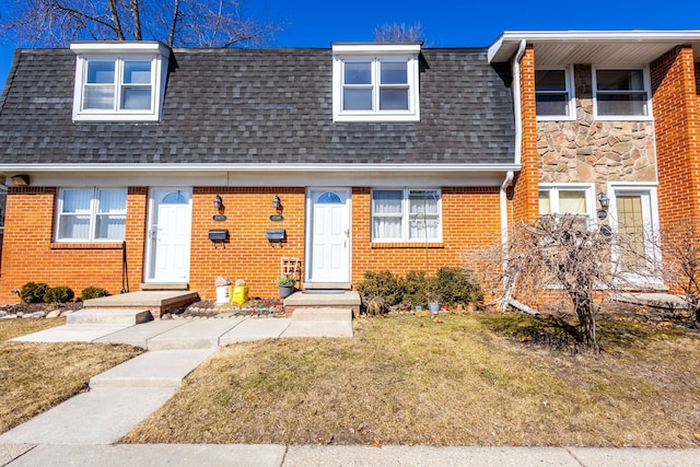 view of property with roof with shingles, mansard roof, a front lawn, stone siding, and brick siding