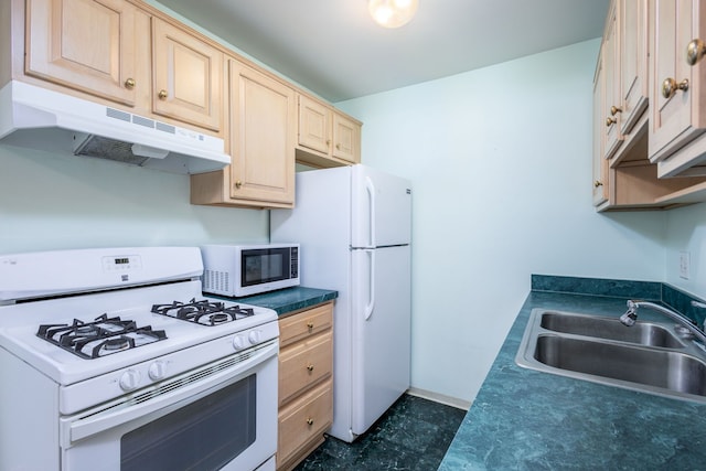 kitchen with dark countertops, under cabinet range hood, light brown cabinetry, white appliances, and a sink