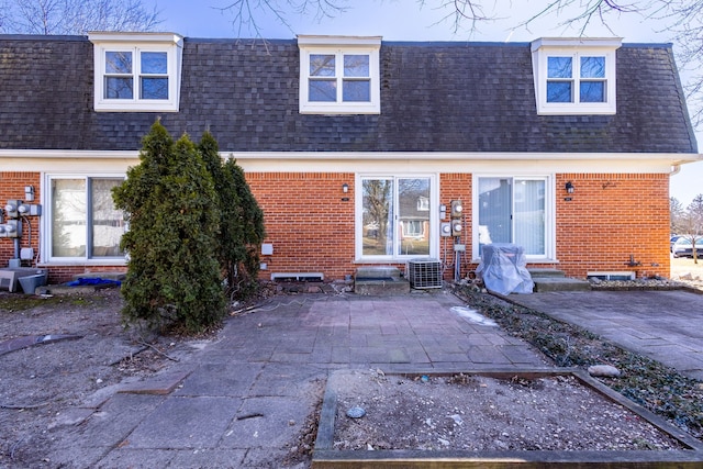 rear view of house with entry steps, brick siding, and a shingled roof