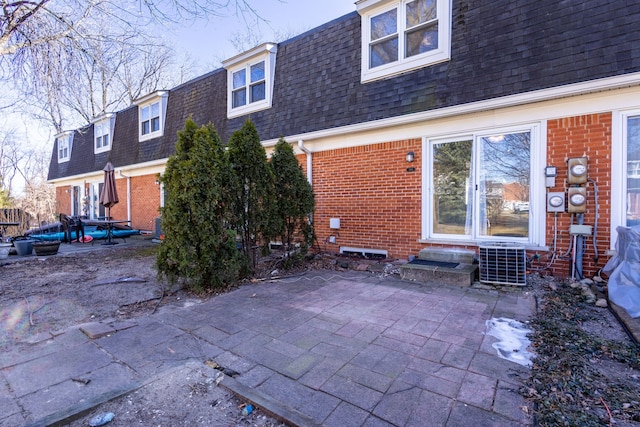 rear view of house featuring entry steps, mansard roof, brick siding, and a shingled roof