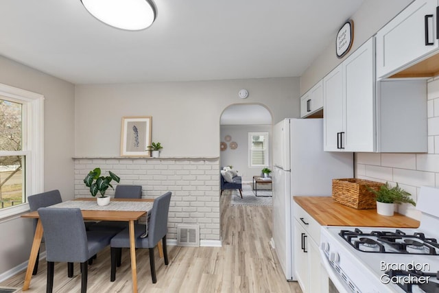 dining space featuring light wood-style floors, arched walkways, visible vents, and baseboards