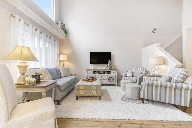 living area featuring wood finished floors, a towering ceiling, and a healthy amount of sunlight