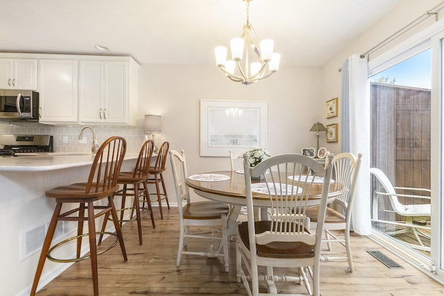 dining area featuring light wood-type flooring, baseboards, visible vents, and a chandelier