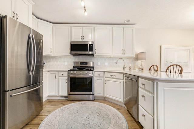 kitchen featuring a peninsula, appliances with stainless steel finishes, a sink, and decorative backsplash