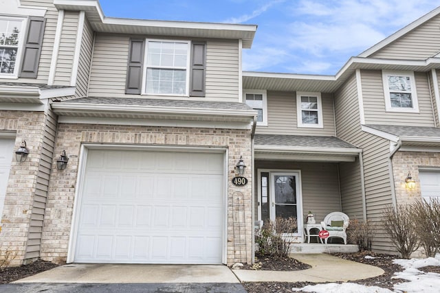 townhome / multi-family property with a garage, driveway, a shingled roof, and brick siding