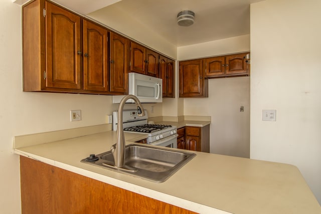 kitchen with white appliances, brown cabinets, a peninsula, light countertops, and a sink