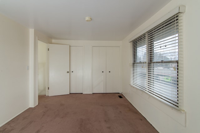 unfurnished bedroom featuring carpet, two closets, and visible vents