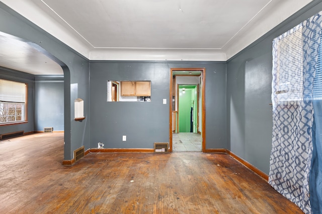 unfurnished room featuring arched walkways, wood-type flooring, visible vents, and baseboards