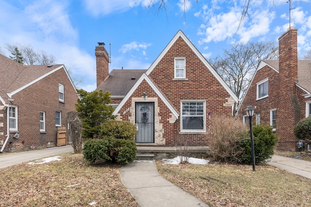 tudor house featuring roof with shingles, a chimney, and brick siding