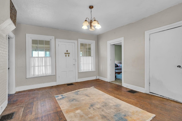 foyer entrance featuring hardwood / wood-style flooring, visible vents, and a notable chandelier