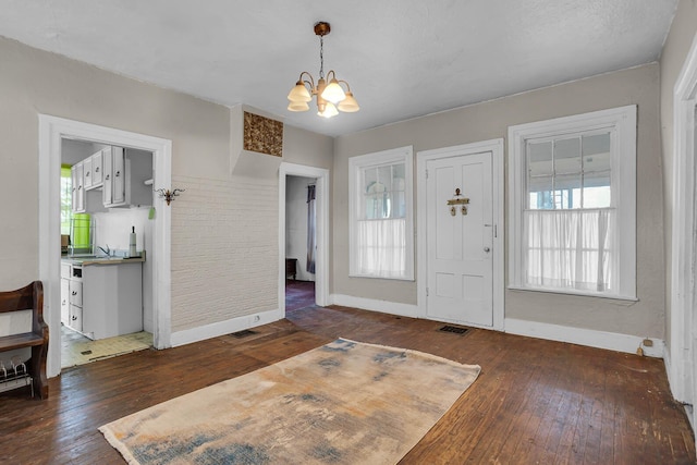 entrance foyer with dark wood-style floors, visible vents, a notable chandelier, and baseboards