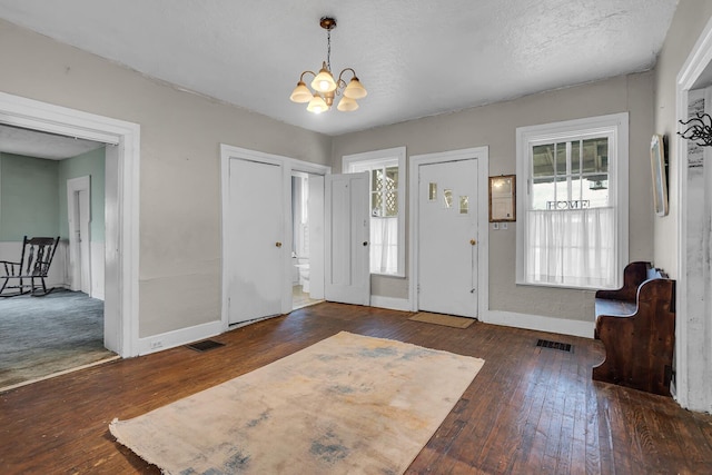 entryway with wood-type flooring, visible vents, baseboards, and an inviting chandelier