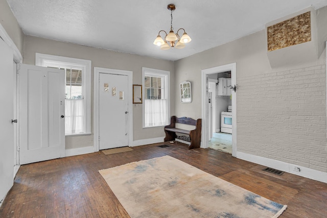 entryway featuring dark wood-style floors, brick wall, visible vents, and a chandelier