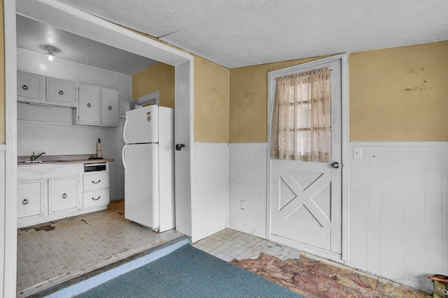 kitchen with wainscoting, wood walls, a sink, and freestanding refrigerator