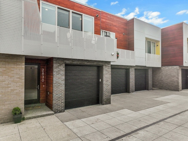 view of front of house with driveway, brick siding, an attached garage, and a balcony