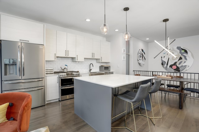 kitchen featuring light countertops, backsplash, appliances with stainless steel finishes, dark wood-type flooring, and a kitchen island