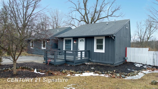 view of front facade with a deck, fence, and roof with shingles