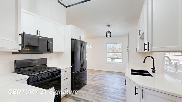 kitchen featuring black appliances, a sink, light countertops, decorative backsplash, and light wood-style flooring