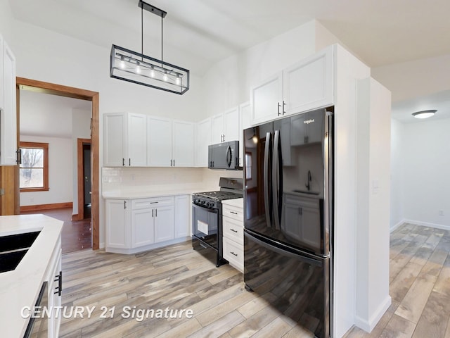 kitchen featuring black appliances, light wood-type flooring, light countertops, white cabinetry, and a towering ceiling