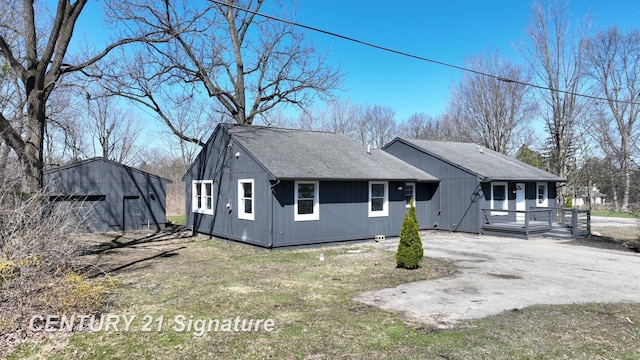 view of front of property featuring an outdoor structure, asphalt driveway, and roof with shingles