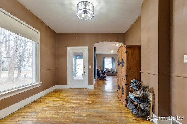 foyer featuring arched walkways, baseboards, and light wood-style floors