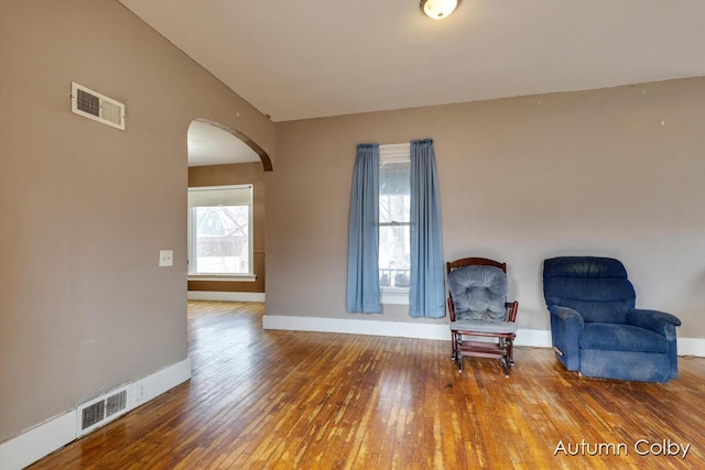 living area with baseboards, visible vents, arched walkways, and hardwood / wood-style floors