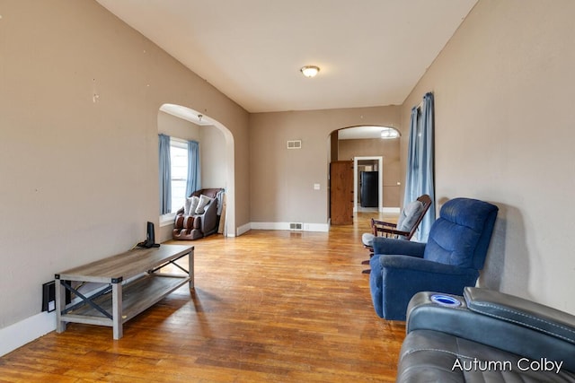 living room with arched walkways, wood finished floors, and visible vents