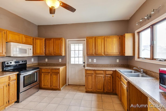 kitchen featuring light tile patterned floors, white microwave, a sink, brown cabinetry, and stainless steel range with electric stovetop