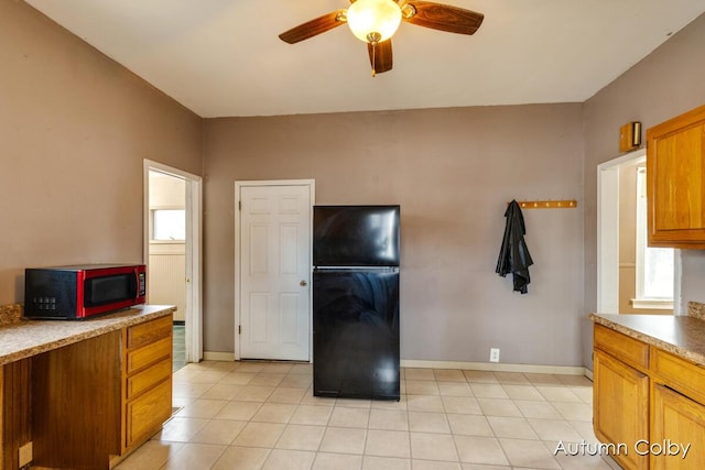 kitchen featuring ceiling fan, light tile patterned floors, brown cabinetry, and freestanding refrigerator