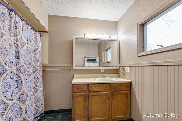 bathroom with tile patterned flooring, vanity, a textured ceiling, and wainscoting