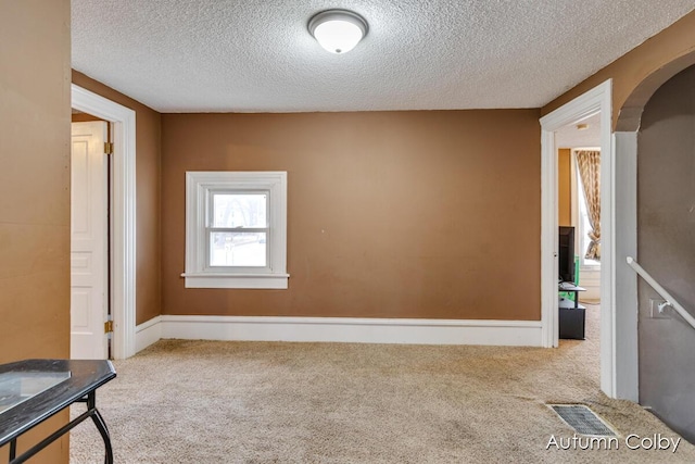 carpeted spare room featuring arched walkways, a textured ceiling, and visible vents