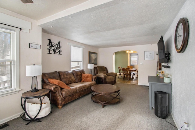 living room with arched walkways, a textured ceiling, carpet flooring, and a wealth of natural light