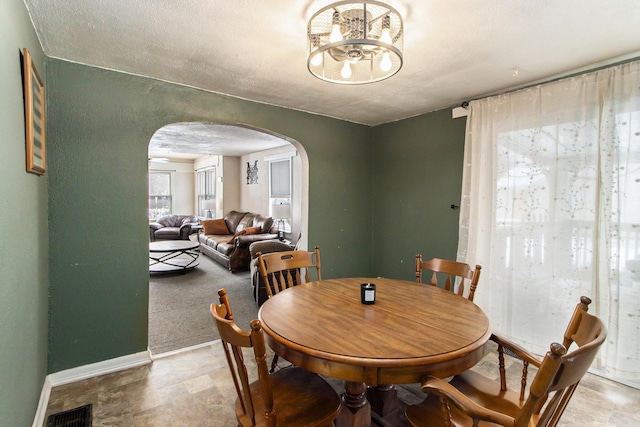 dining space featuring visible vents, arched walkways, baseboards, an inviting chandelier, and a textured ceiling